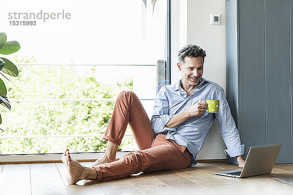 Reifer Mann entspannt sich zu Hause bei einer Tasse Kaffee  mit Laptop