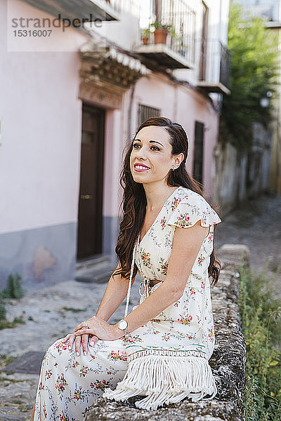 Porträt einer lächelnden Frau in blumengeschmücktem Kleid an einer Wand sitzend  Granada  Spanien