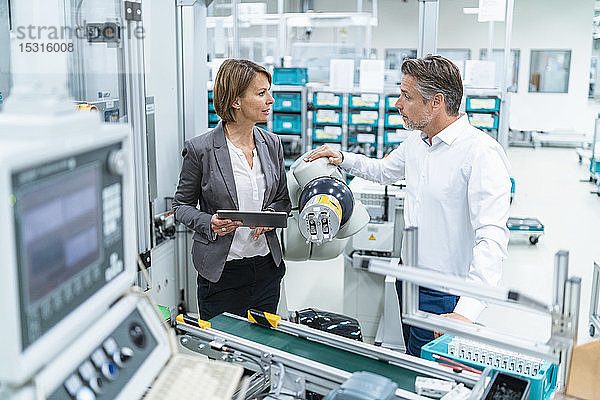 Geschäftsfrau und Mann unterhalten sich an einem Montageroboter in einer Fabrik
