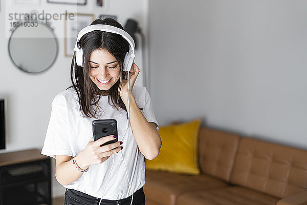 Glückliche junge Frau mit Smartphone und Kopfhörern zu Hause