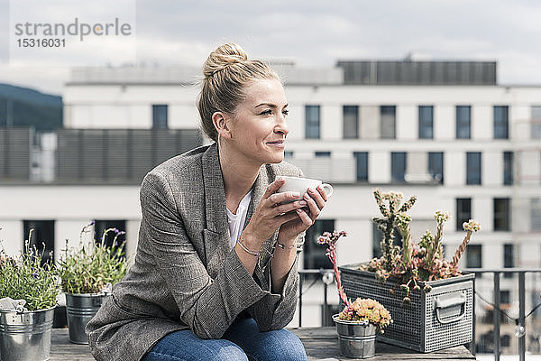 Geschäftsfrau mit Kaffeetasse sitzt auf der Dachterrasse und macht eine Pause