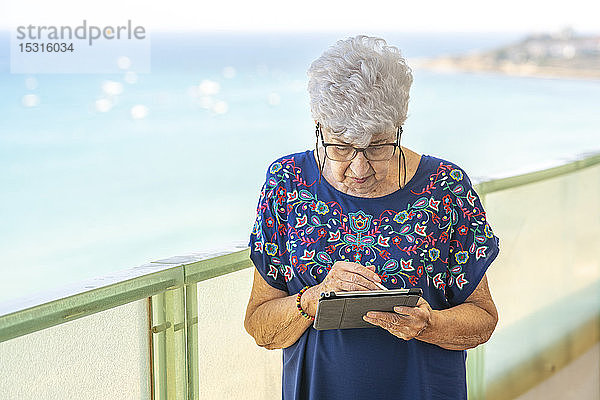Ältere Frau benutzt eine Tablette auf einer Terrasse