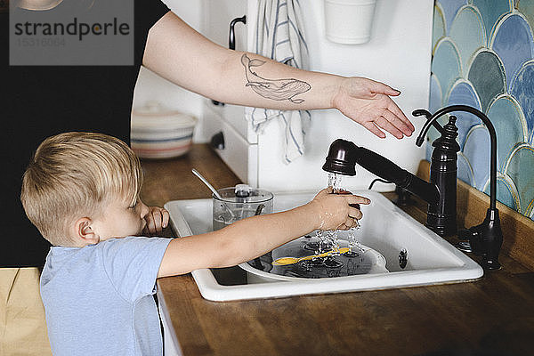 Kleiner Junge wäscht Pfirsich in der Küche mit der Hilfe seiner Mutter