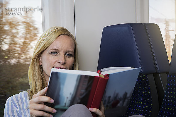 Frau sitzt in einem Zug und liest ein Buch