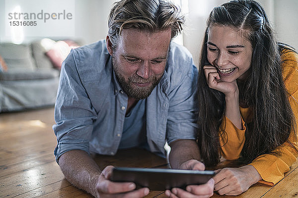 Glückliches Paar liegt zu Hause auf dem Boden und schaut auf die Tablette