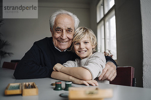 Porträt eines glücklichen Uhrmachers und seines Enkels am Tisch sitzend