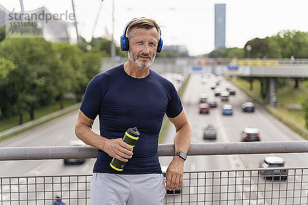 Sportlicher Mann mit Trinkflasche und Kopfhörer auf einer Brücke