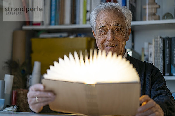 Älterer Mann mit leuchtendem Buch zu Hause
