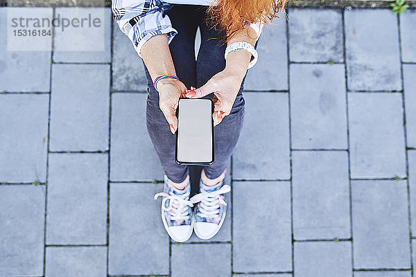 Draufsicht einer Frau  die ein Smartphone benutzt  während sie im Freien sitzt