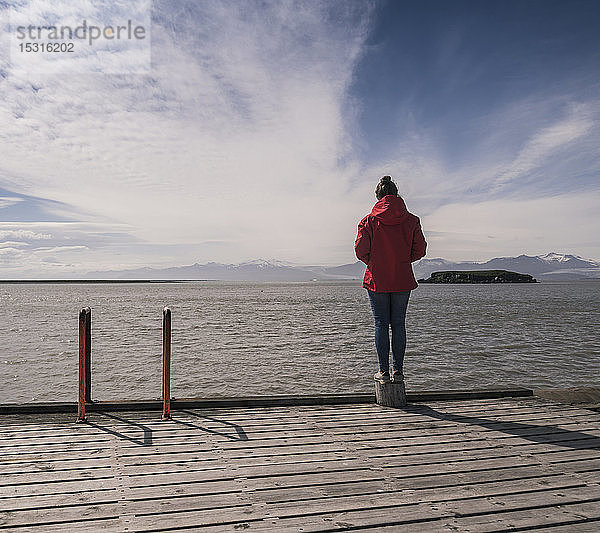 Junge Frau steht auf einem Steg und schaut auf das Meer  Südost-Island