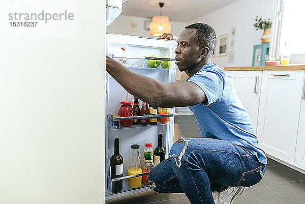 Junger Mann schaut zu Hause in den Kühlschrank in der Küche