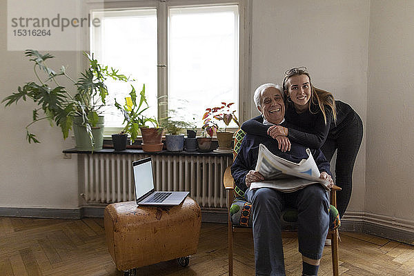 Porträt einer glücklichen jungen Frau und eines älteren Mannes mit Zeitung zu Hause