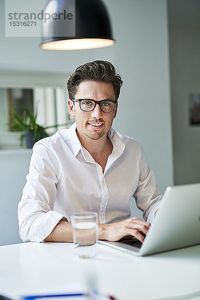 Porträt eines lächelnden Geschäftsmannes mit Laptop im Büro
