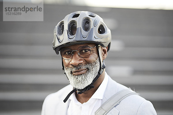 Porträt eines lächelnden reifen Geschäftsmannes mit grauem Bart  der einen Fahrradhelm und eine Brille trägt