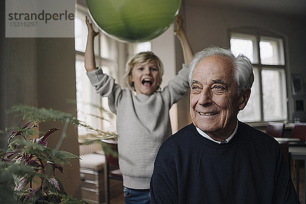 Porträt eines lächelnden älteren Mannes mit Enkel  der im Hintergrund einen Ballon hält