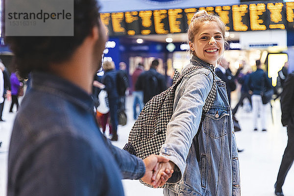 Porträt einer glücklichen jungen Frau Hand in Hand mit seinem Freund am Bahnhof