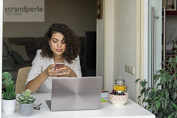Junge Frau benutzt Handy und Laptop am Schreibtisch