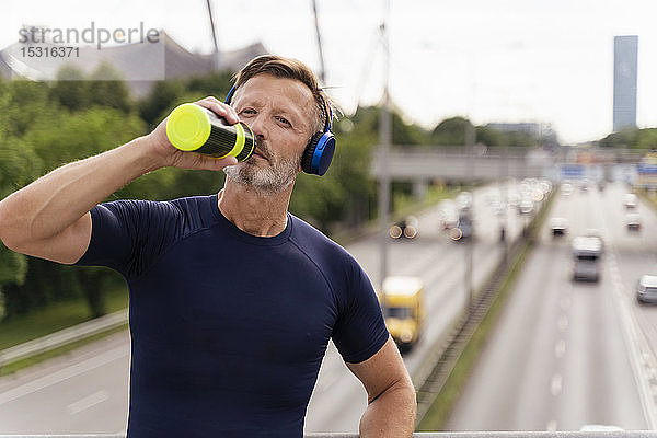 Sportlicher Mann mit Trinkflasche und Kopfhörer auf einer Brücke