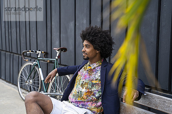 Stilvoller Mann mit Fahrrad auf einer Bank sitzend