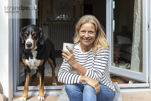 Porträt einer glücklichen reifen Frau  die mit Kaffeetasse auf der Terrasse sitzt