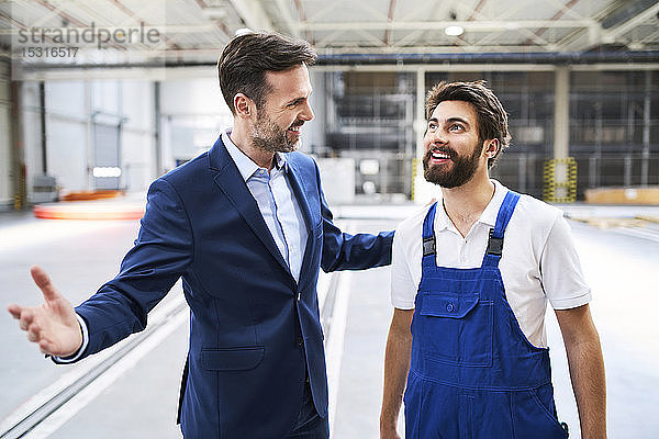 Glücklicher Geschäftsmann und Arbeiter in einer Fabrik