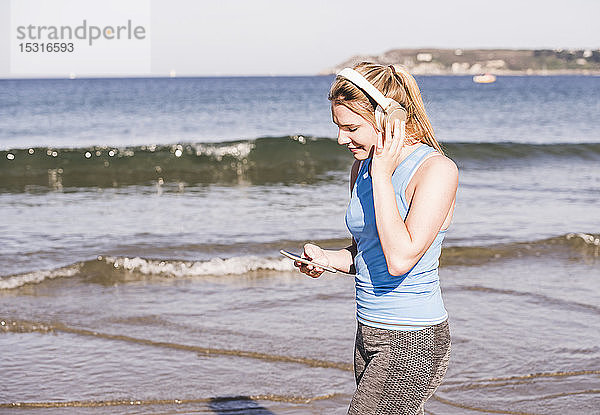 Joggerin am Strand  mit Smartphone und Kopfhörern