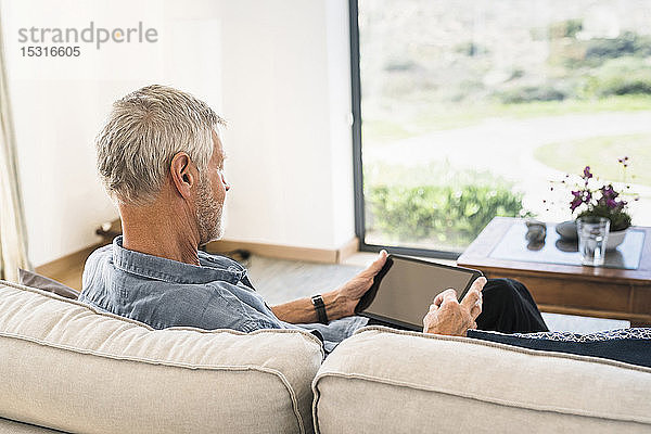 Älterer Mann benutzt Tablette auf Couch zu Hause