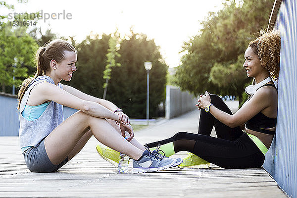Zwei sportliche junge Frauen entspannen sich nach dem Training auf einer Brücke