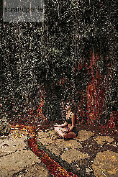 Junge Frau meditiert an einem Wasserfall
