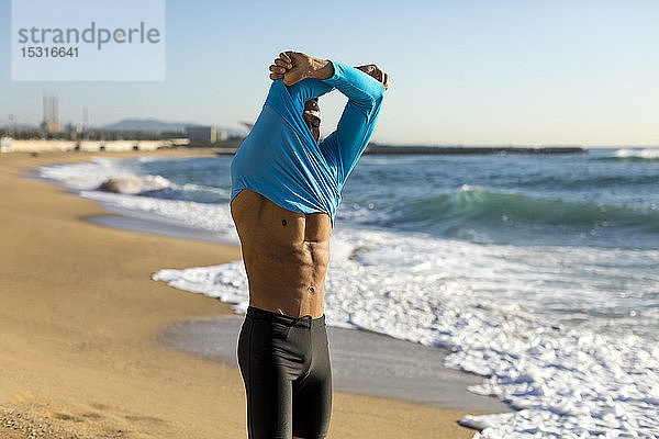 Mann zieht während eines Trainings am Strand sein Hemd aus