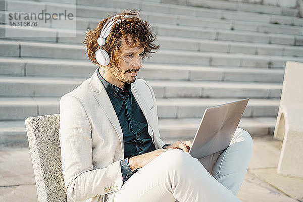Geschäftsmann mit Kopfhörern  der im Freien am Laptop arbeitet