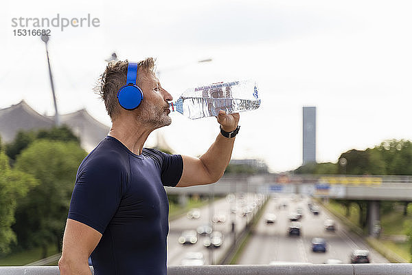 Sportlicher Mann mit Kopfhörern und Trinkwasser auf einer Brücke