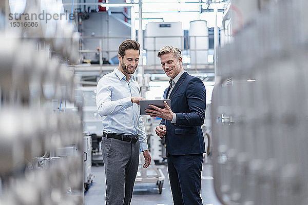 Zwei Geschäftsleute mit Tablette im Gespräch in einer modernen Fabrik