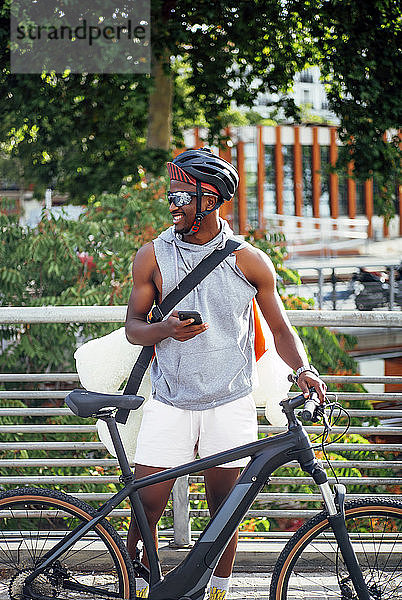 Fröhlicher Fahrradkurier mit Handy sieht sich um
