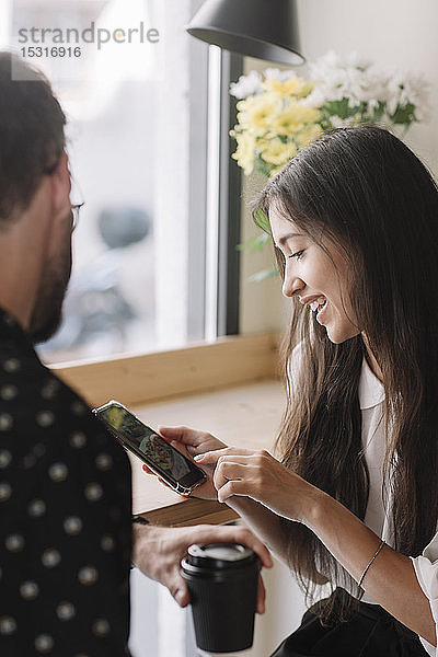 Junges Paar mit Einwegbecher und Smartphone in einem Cafe