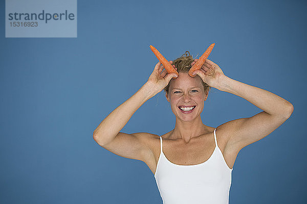 Lächelnde blonde Frau mit Karotten in der Hand  blauer Hintergrund