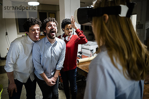 Spielerische Kollegen betrachten Frau mit VR-Brille im Büro