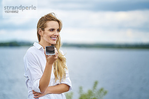 Glückliche Frau benutzt Handy am Seeufer