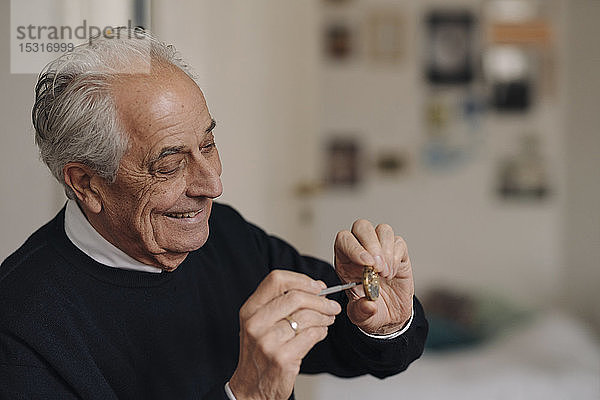 Lächelnder älterer Mann  der zu Hause eine Uhr repariert