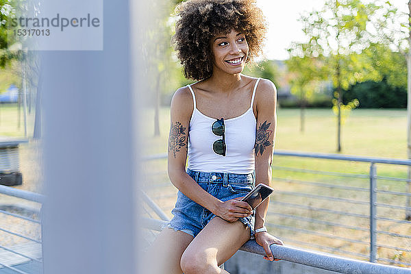Porträt einer tätowierten jungen Frau mit Smartphone im Sommer