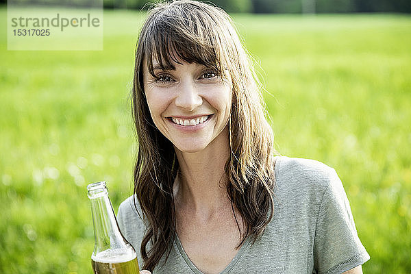Porträt einer lächelnden brünetten Frau mit einer Bierflasche im Freien