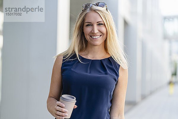 Porträt einer lächelnden blonden Geschäftsfrau mit Kaffee zum Mitnehmen im Sommer