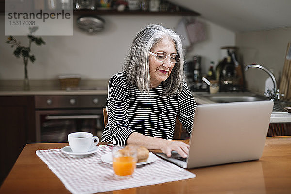 Porträt einer älteren Frau mit Laptop am Frühstückstisch