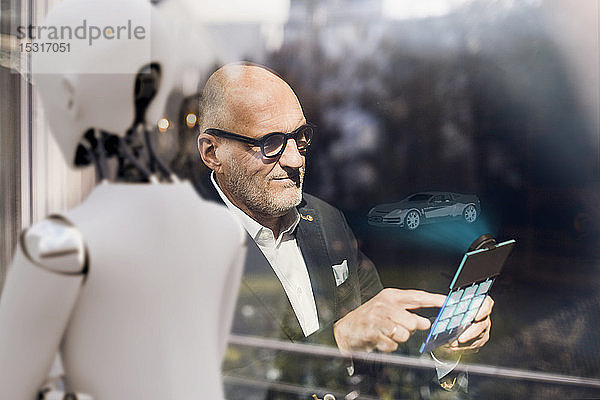 Leitender Geschäftsmann mit digitalem Tablet  auf der Suche nach computergesteuerten Autos