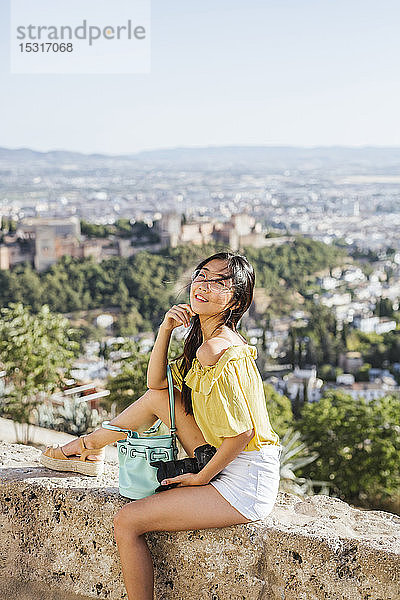Lächelnde junge Frau mit Kamera an einer Wand in der Alhambra  Granada  Spanien