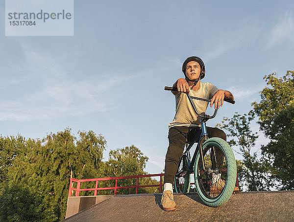 Junger Mann mit BMX-Rad im Skatepark bei einer Pause
