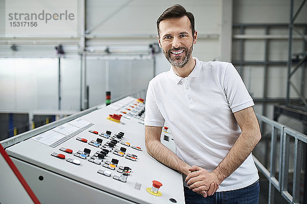 Porträt eines lächelnden Mannes  der an einer Schalttafel in einer Fabrik steht