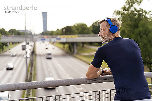 Sportlicher Mann steht auf einer Brücke und trägt Kopfhörer