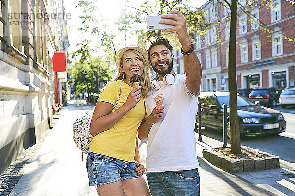 Glückliches junges Paar  das sich beim Eisessen in der Stadt ein Selfie gönnt