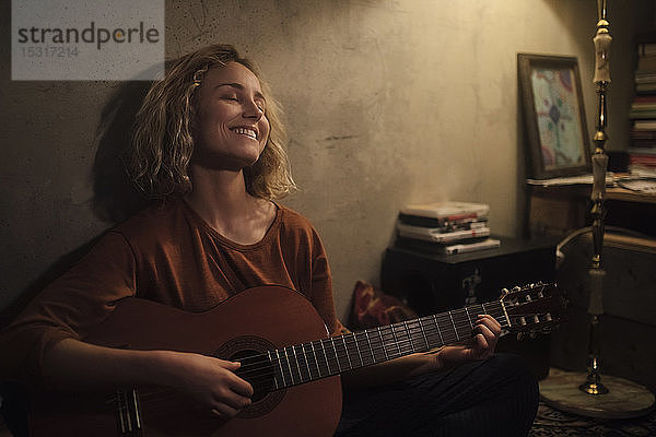 Glückliche junge Frau spielt zu Hause Gitarre